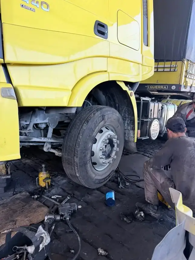 Mecânico da Faísca trabalhando na roda dianteira de um Iveco amarelo